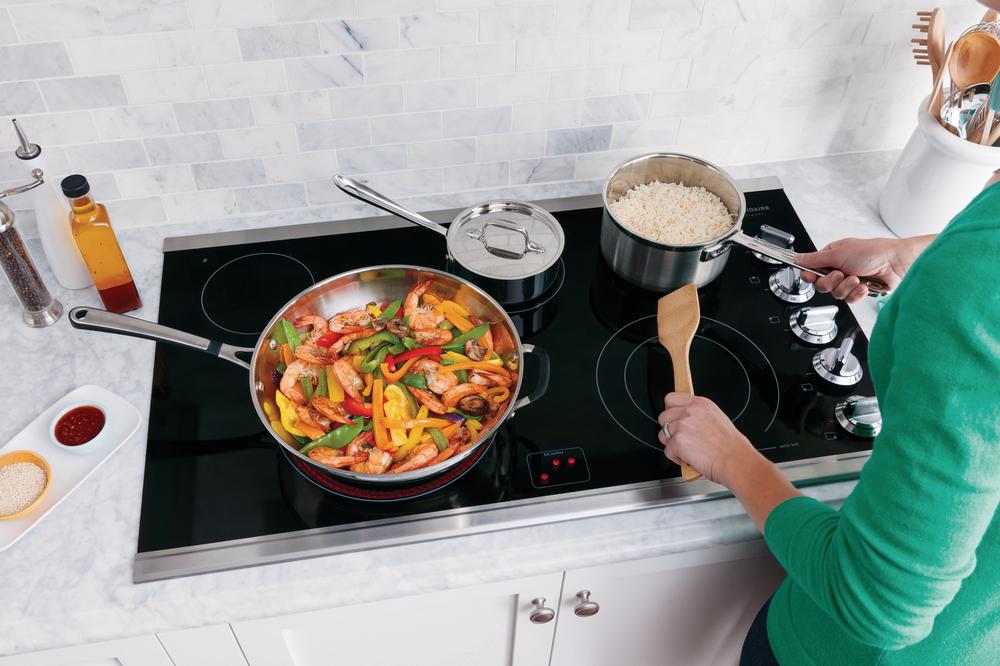 closeup of woman’s hands cooking pans over Frigidaire Professional induction cooktop