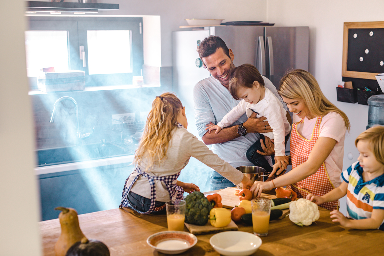 family assembles around kitchen island as they cook together
