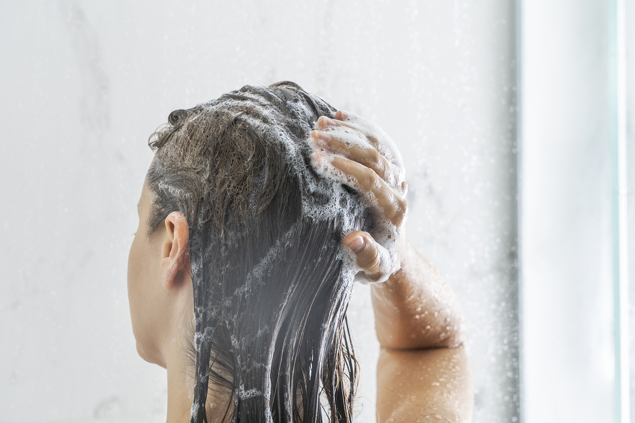 young woman applying shampoo on her hair in bathroom