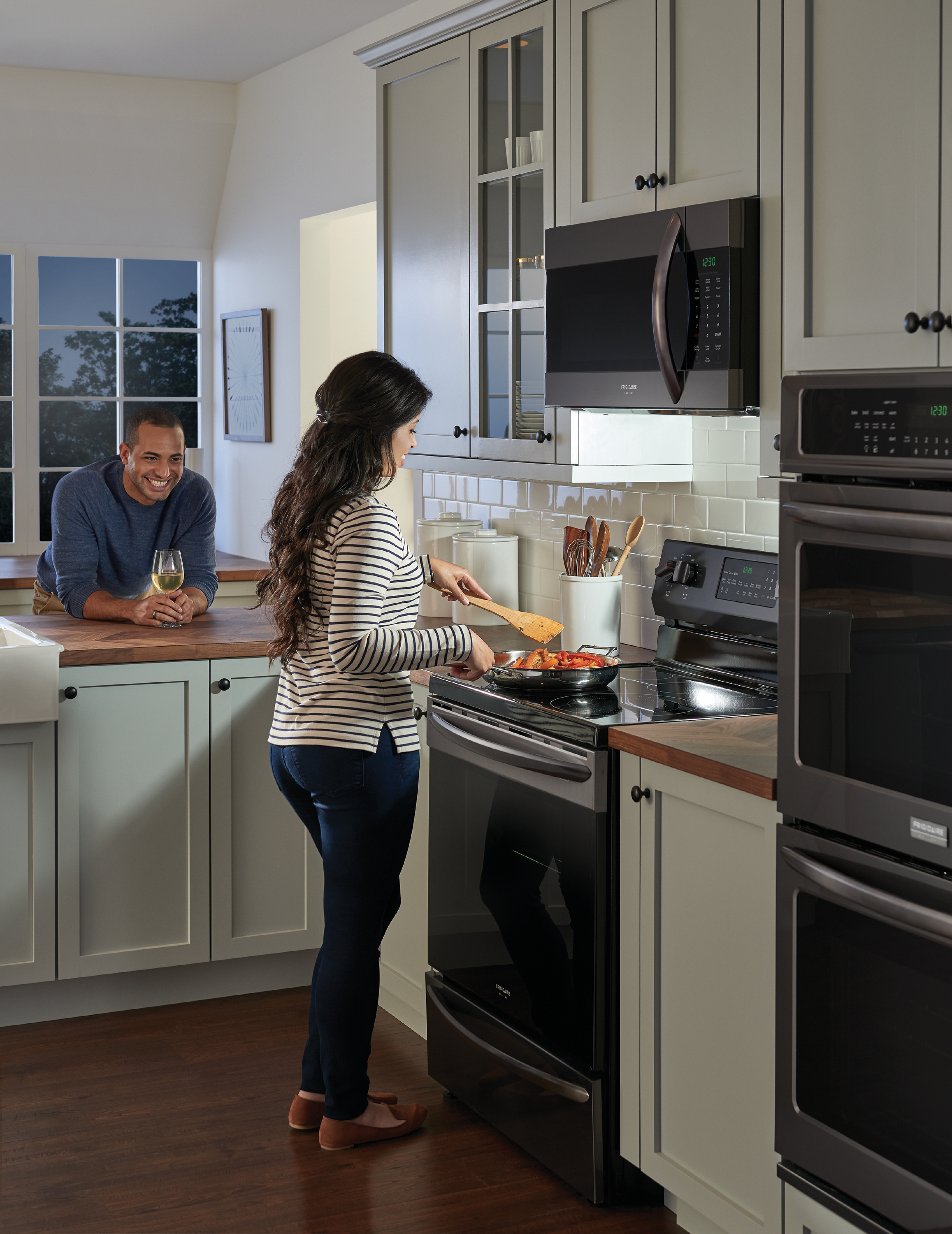 Woman cooking on a Frigidaire electric range while a man smiles and watches from a kitchen island 