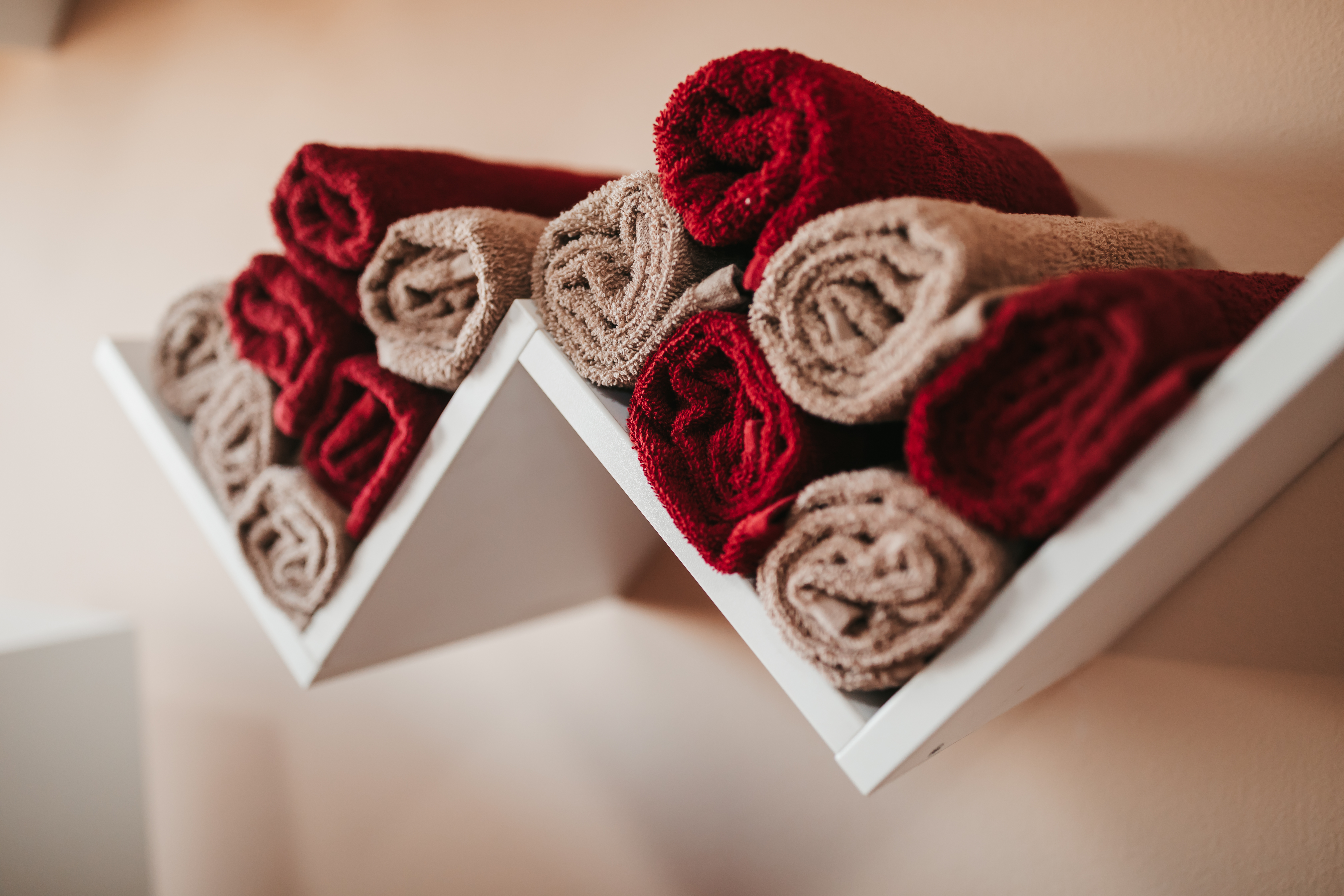 Red and brown rolled hand towels organized on floating diagonal wall shelves 
