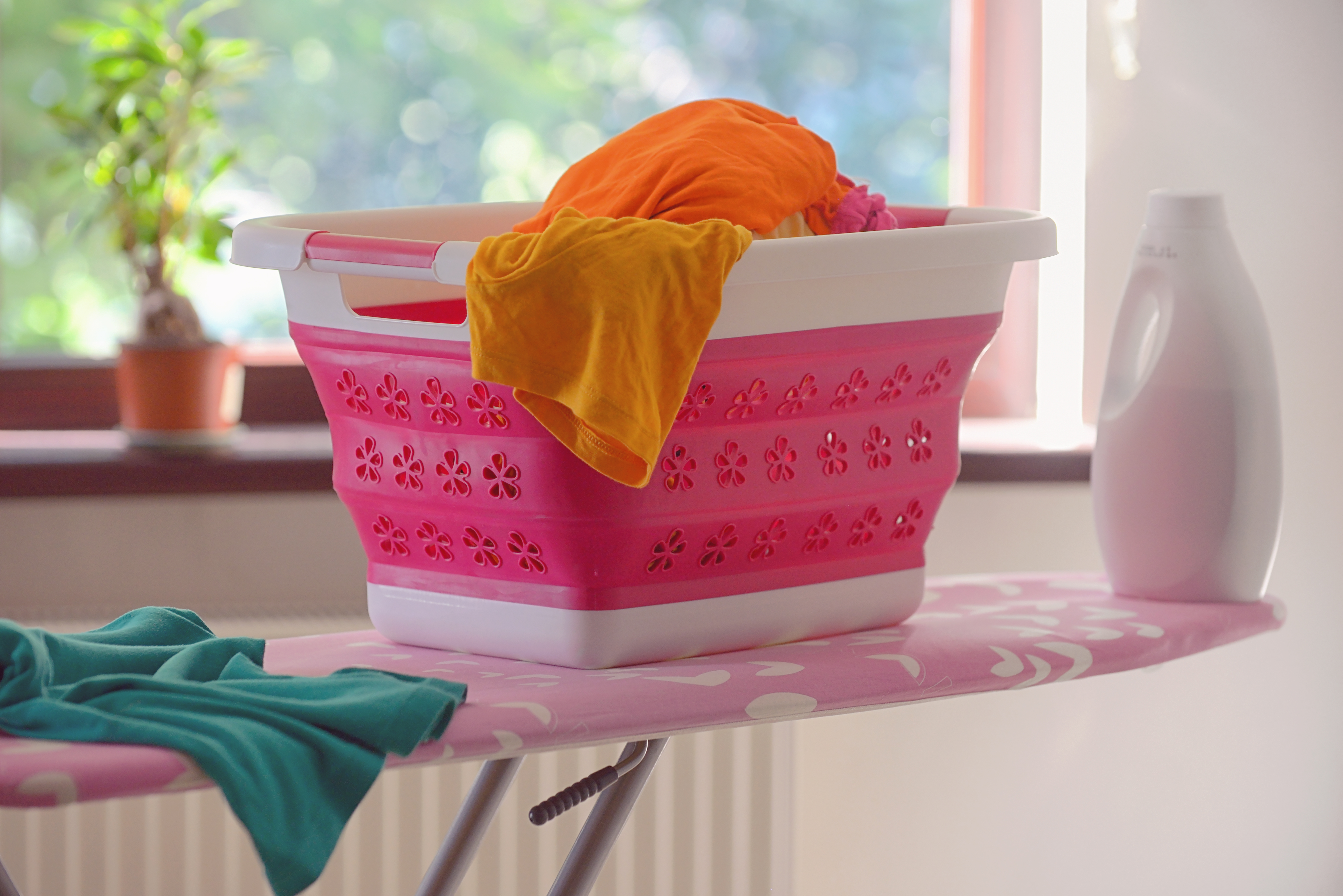 A pink collapsible laundry basket on an ironing board 