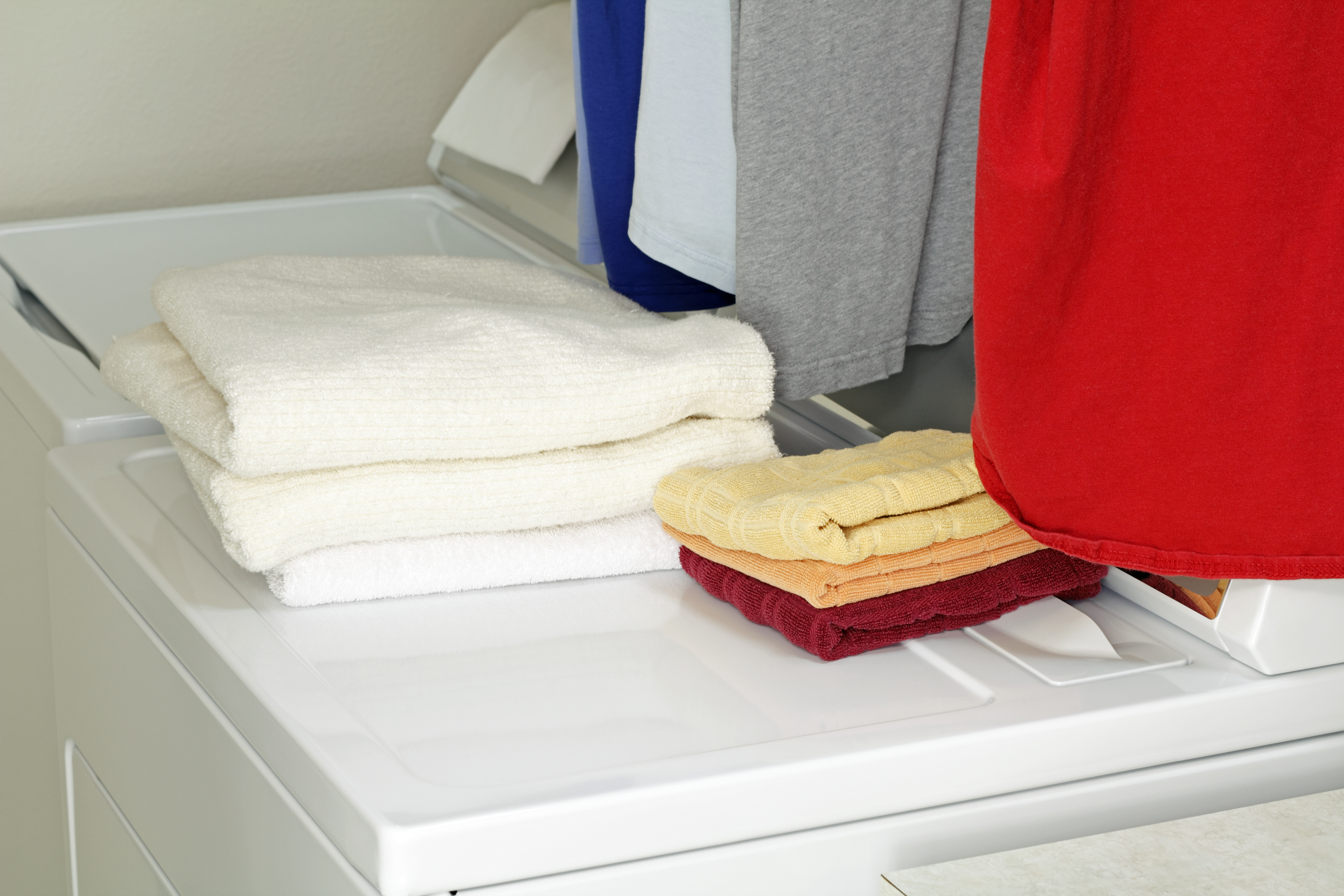 A matching top load washer and dryer with folded towels and hanging clothes 