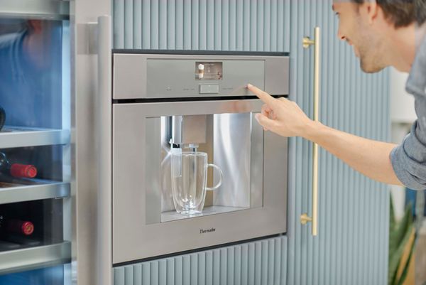 man gets coffee from Thermador built-in coffee machine in stainless steel