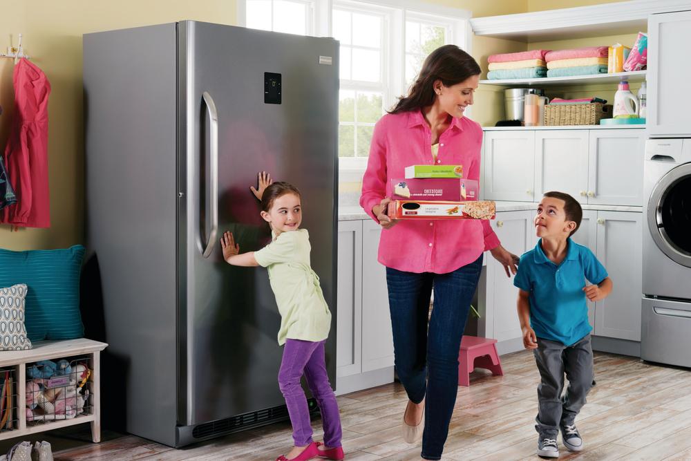 smiling mother retrieves frozen meals from Frigidaire Gallery upright freezer