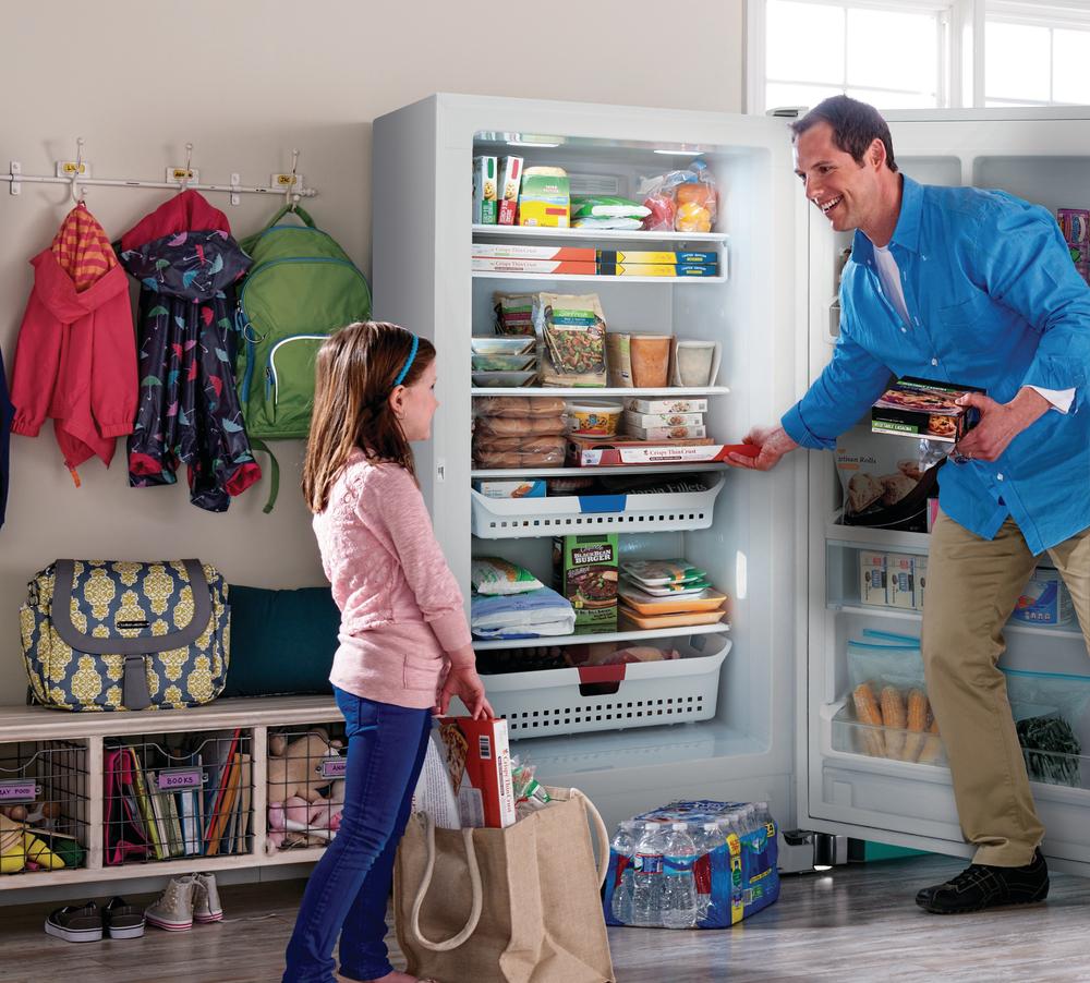 father organizes groceries with daughter in Frigidaire upright freezer
