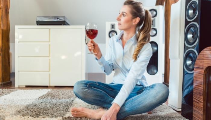 Woman with wine glass sitting on carpet in front of speakers