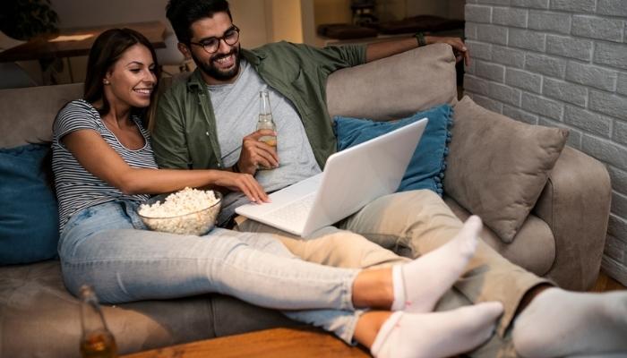 couple is lounging on the sofa and watching movies on a laptop