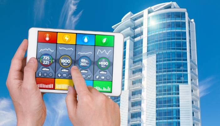 A concept image of someone holding a smart control panel in front of a commercial building