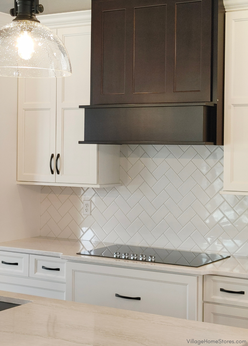 Image of white kitchen cabinets and cherry stained wood hood with electric cooktop and white subway tile backsplash