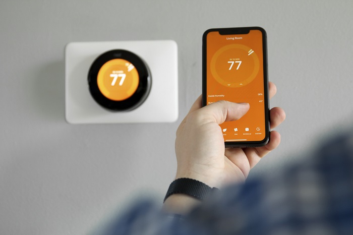 Man uses a mobile phone with smart home app in modern living room to adjust temperature. 