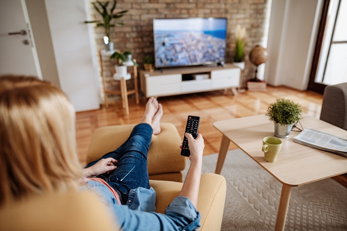 Woman sitting in a chair with her feet up watching tv with the remote control in her hand. 