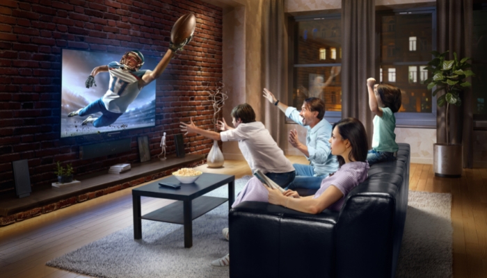 Group of people watching intense Super Bowl game with player coming out of the screen