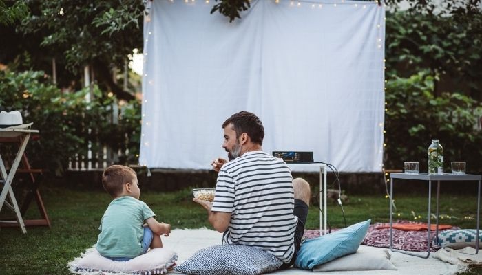 Father and son sitting in backyard and looking movie setup