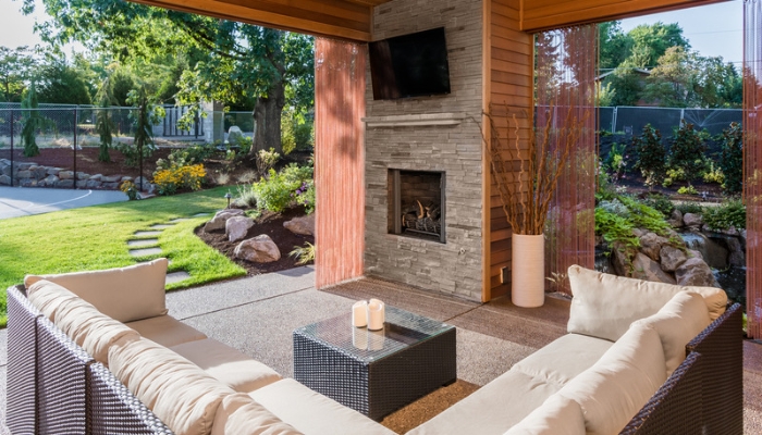 An outdoor TV space with wood features and a square cream couch and fireplace