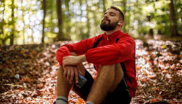 Man listening to ear buds while taking a break on his nature hike in the woods