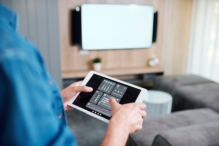 Hands of a man holding tablet with smart remote control system while adjusting volume. 