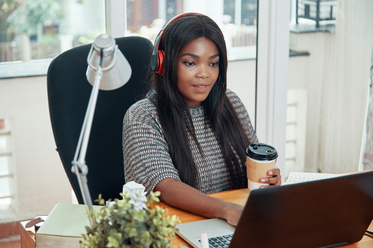 Woman wears headphones as she works from home at her desk with computer