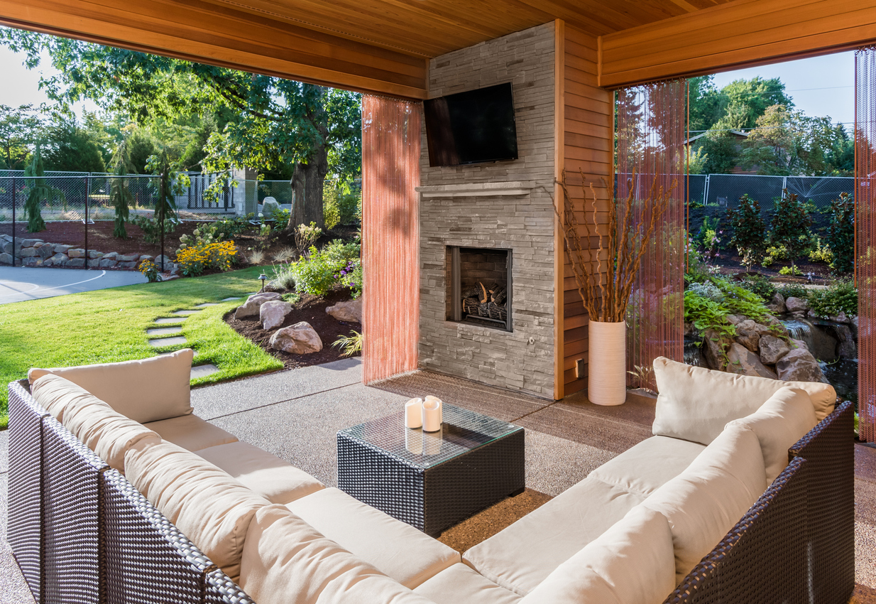 covered patio with fireplace, tv, and couch, with view of lush green grass and landscaping