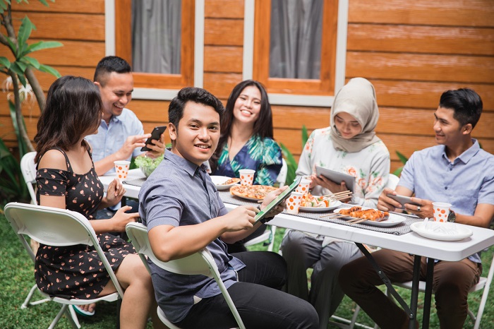 Man on a tablet looks at camera while his backyard-dinner guests use wifi on their phones