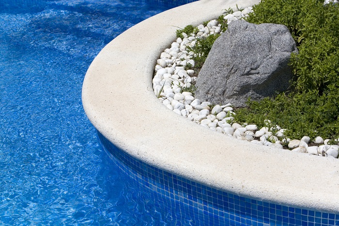 Swimming pool border with water in motion, plants and rocks. The big rock is a poolside speaker.