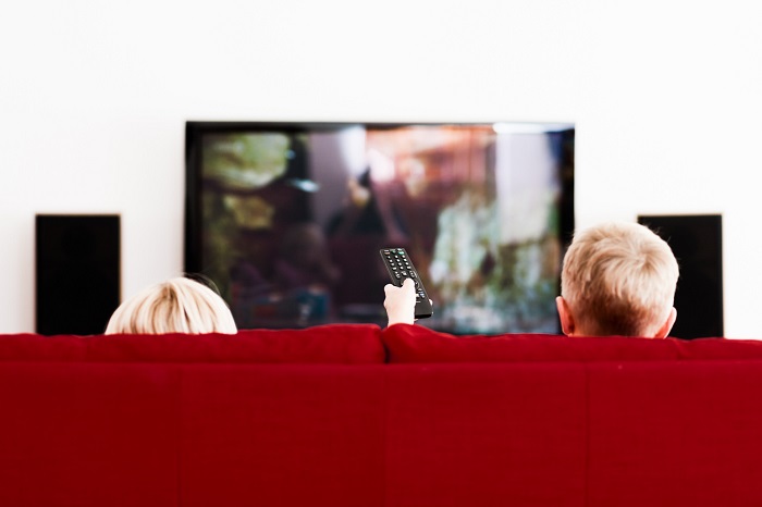 Two blonde siblings watch their home theater tv with a sound system in view