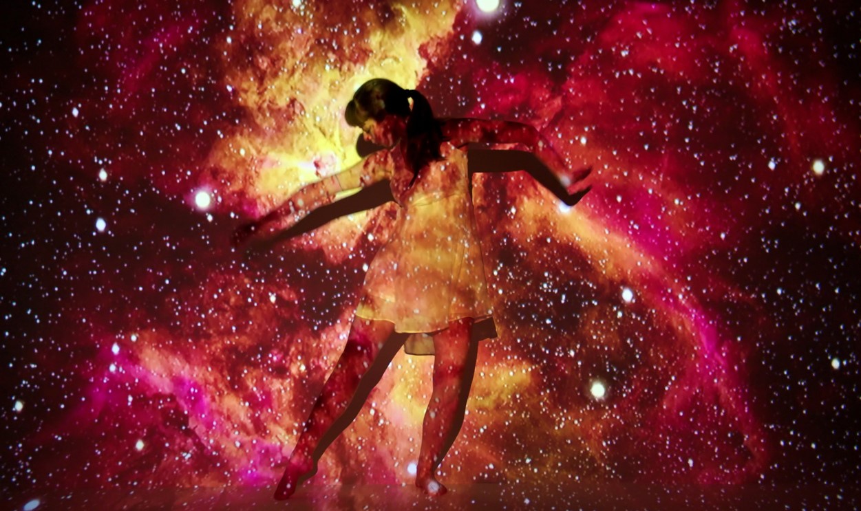 young woman poses in front of projector screen with nebula projection