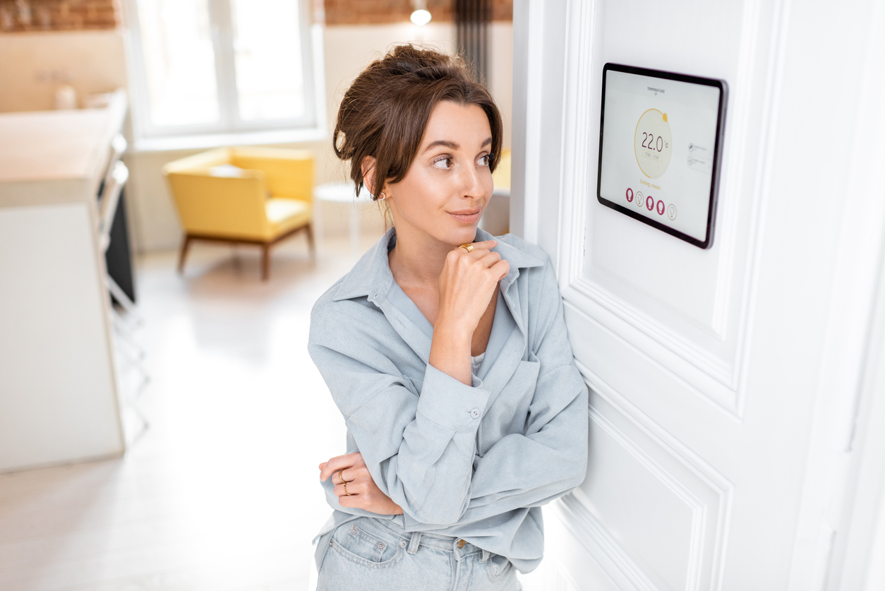 Woman talks at wall-mounted smart thermostat controller