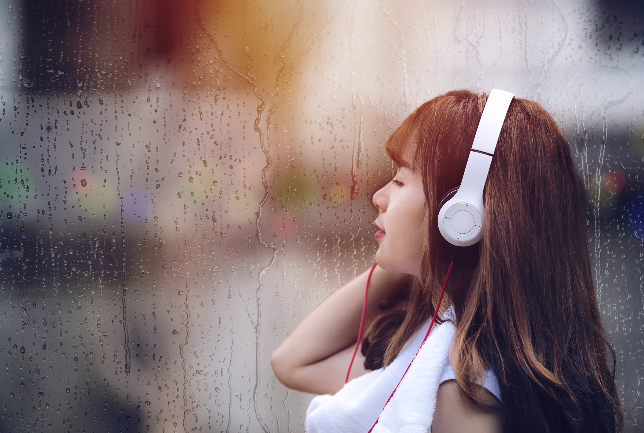 woman with headphones staring out the window during a rainy day
