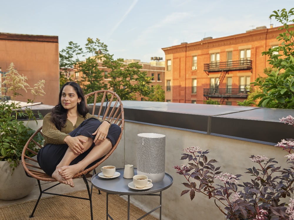 woman sits on rooftop patio listening to a wireless Sonos speaker
