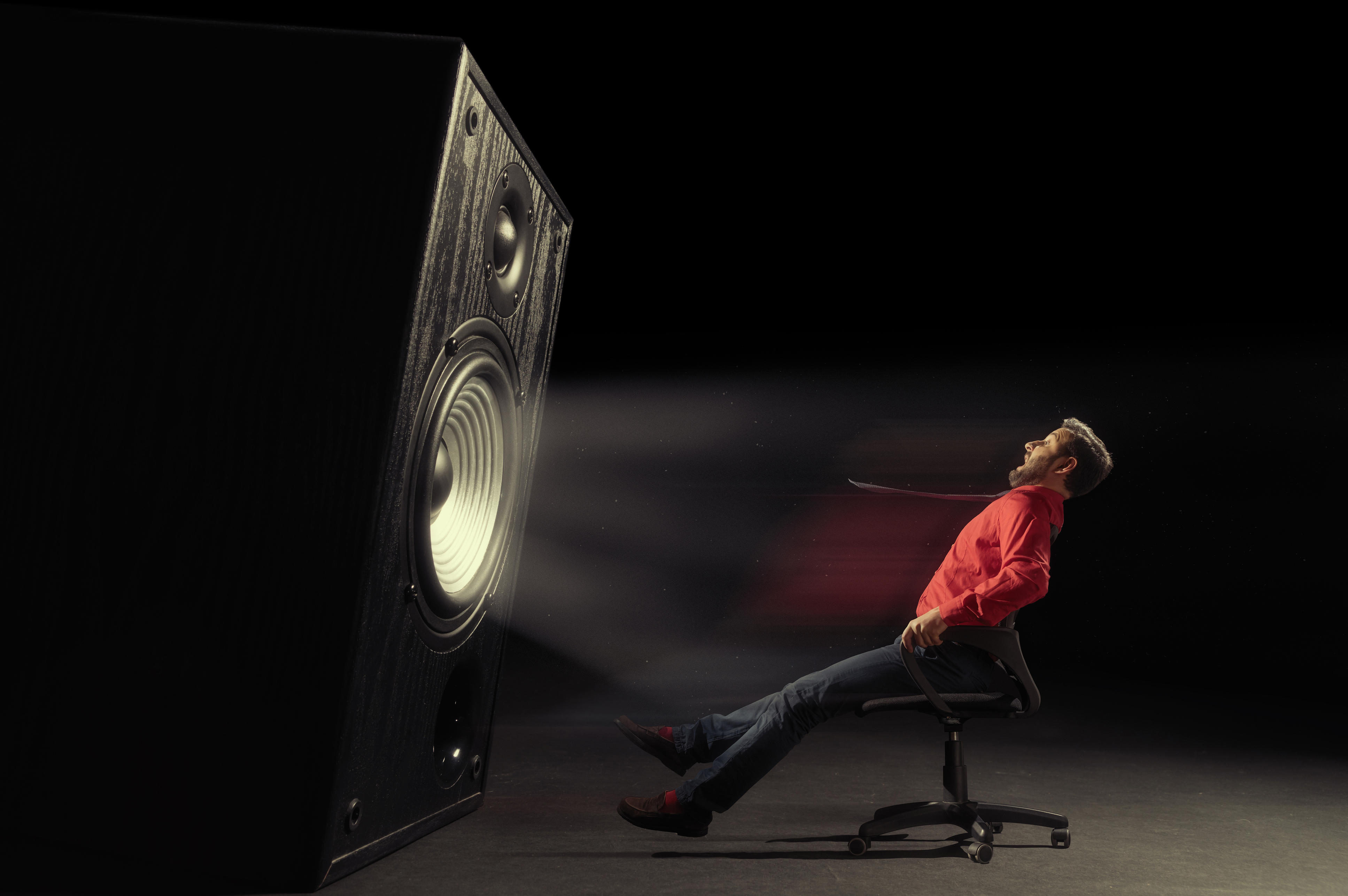 Man in red shirt seated in chair being blasted back by giant subwoofer speaker