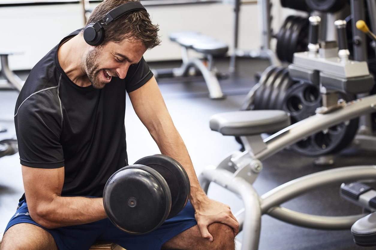 man lifts dumbbell in gym while listening to music on headphones