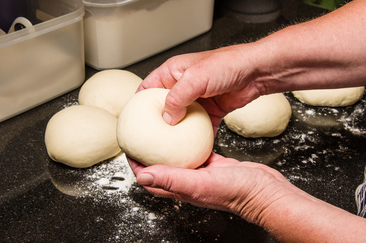 a baker’s hands poke holes in bagel dough