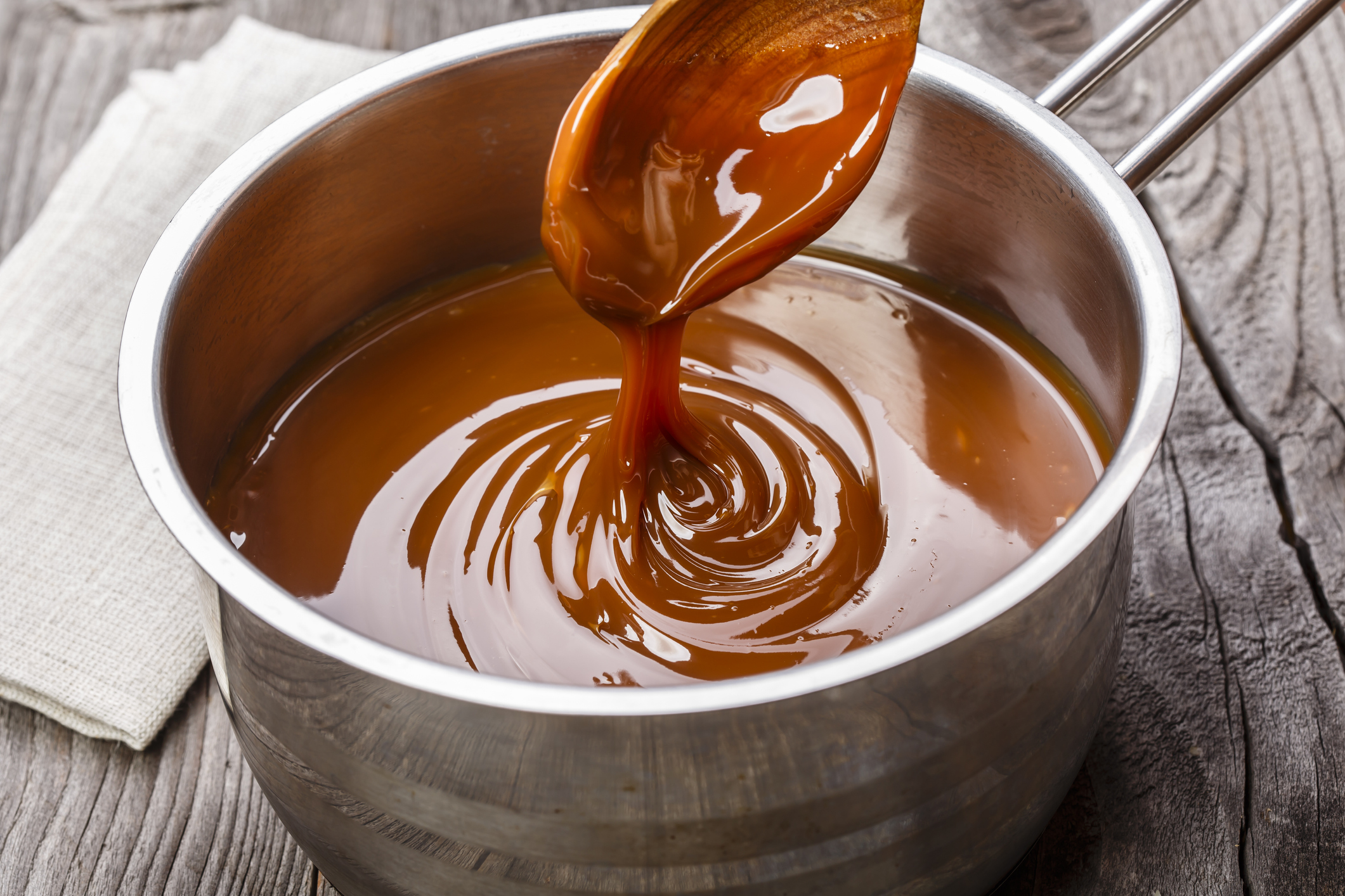 Shot of spoon dipping into saucepan full of caramel sauce