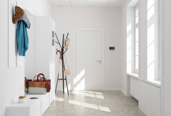front view of a white entryway area with white cabinets, a black coat rack, and miscellaneous items like purses, jackets, and an umbrella stored around.