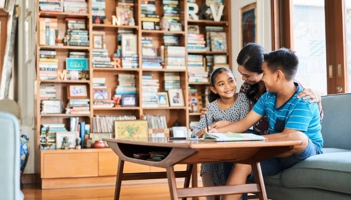 mother, son, and daughter smiling on at worktable in front huge bookshelf