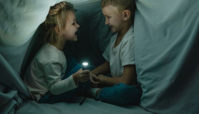 Two kids under a blanket fort with a flashlight
