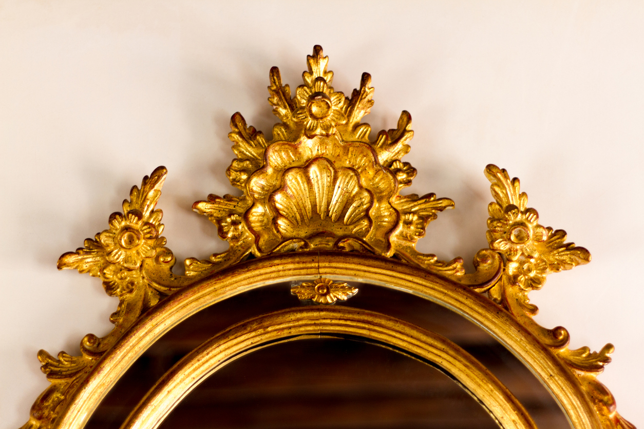 closeup of baroque antique gilded mirror against an off-white wall