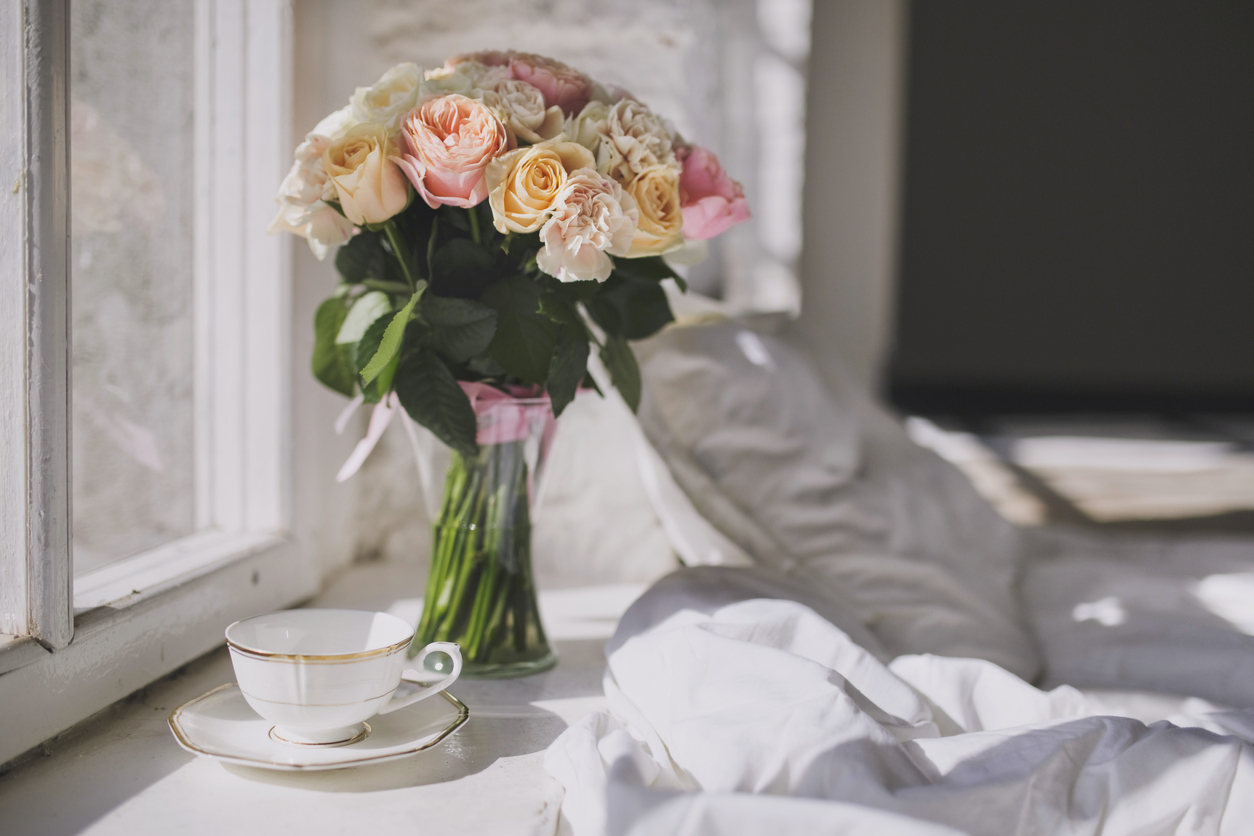 bouquet of pink roses in a glass vase is perched on windowsill next to bed