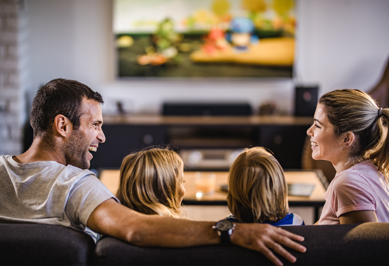 father, mother, brother, and sister enjoying a movie on a big-screen TV