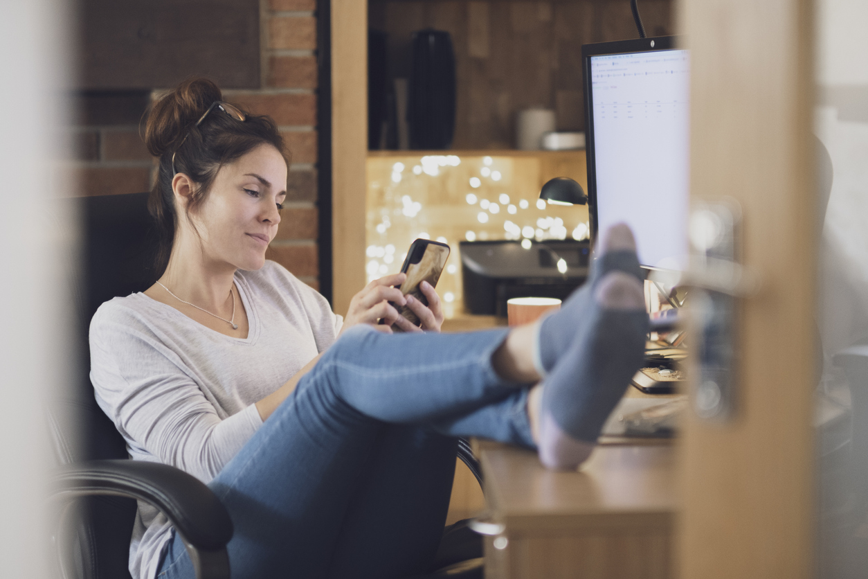 woman in jeans browsed smart phone while she props her legs on a desk