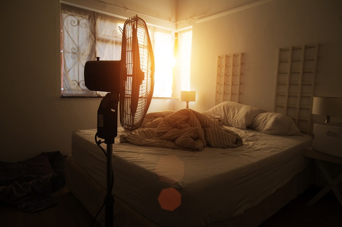 Bedroom filled with early morning sun focused on a fan with a bed in the background.