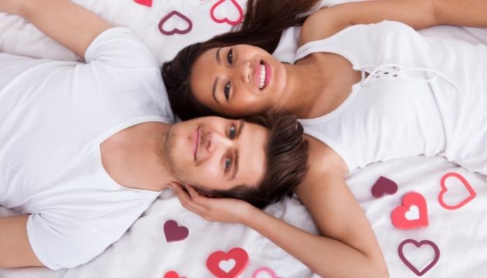 Couple laying down on bed with hearts around them