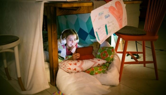 Kid with headphones in pillow fort under a table 