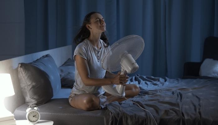 Woman sitting on bed holding fan in front of face