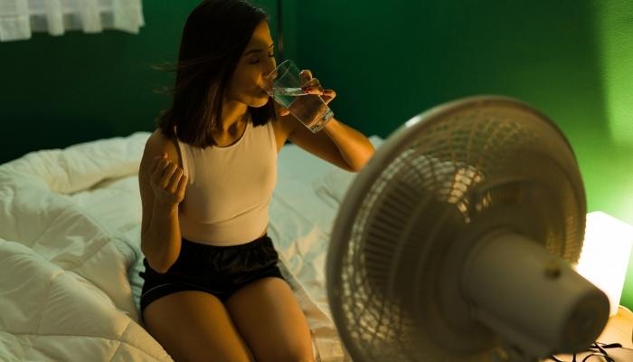 woman in bed drinking water in front of fan