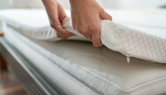 hands placing a mattress topper on bed