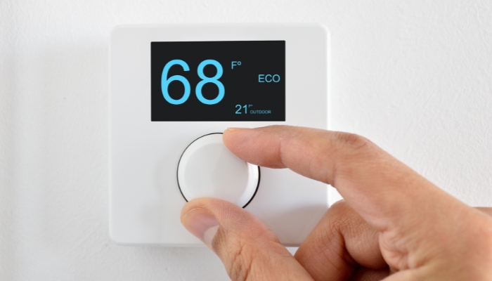 Closeup of hand adjusting thermostat to 68 degrees F