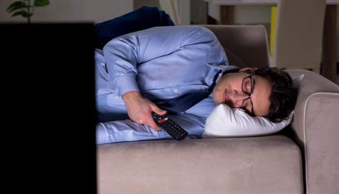 Fully dressed man sleeping on a couch in front of a TV