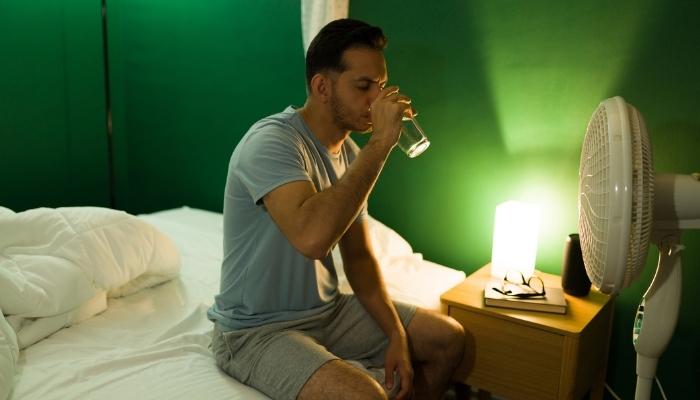 Man drinking water in front of fan in the middle of the night